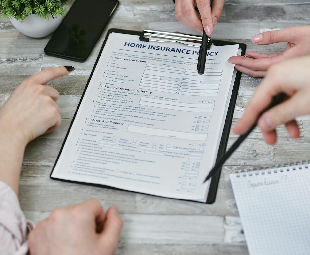 Three individuals collaborating on a home insurance policy document. Elements include a clipboard, notes, and pointing hands.